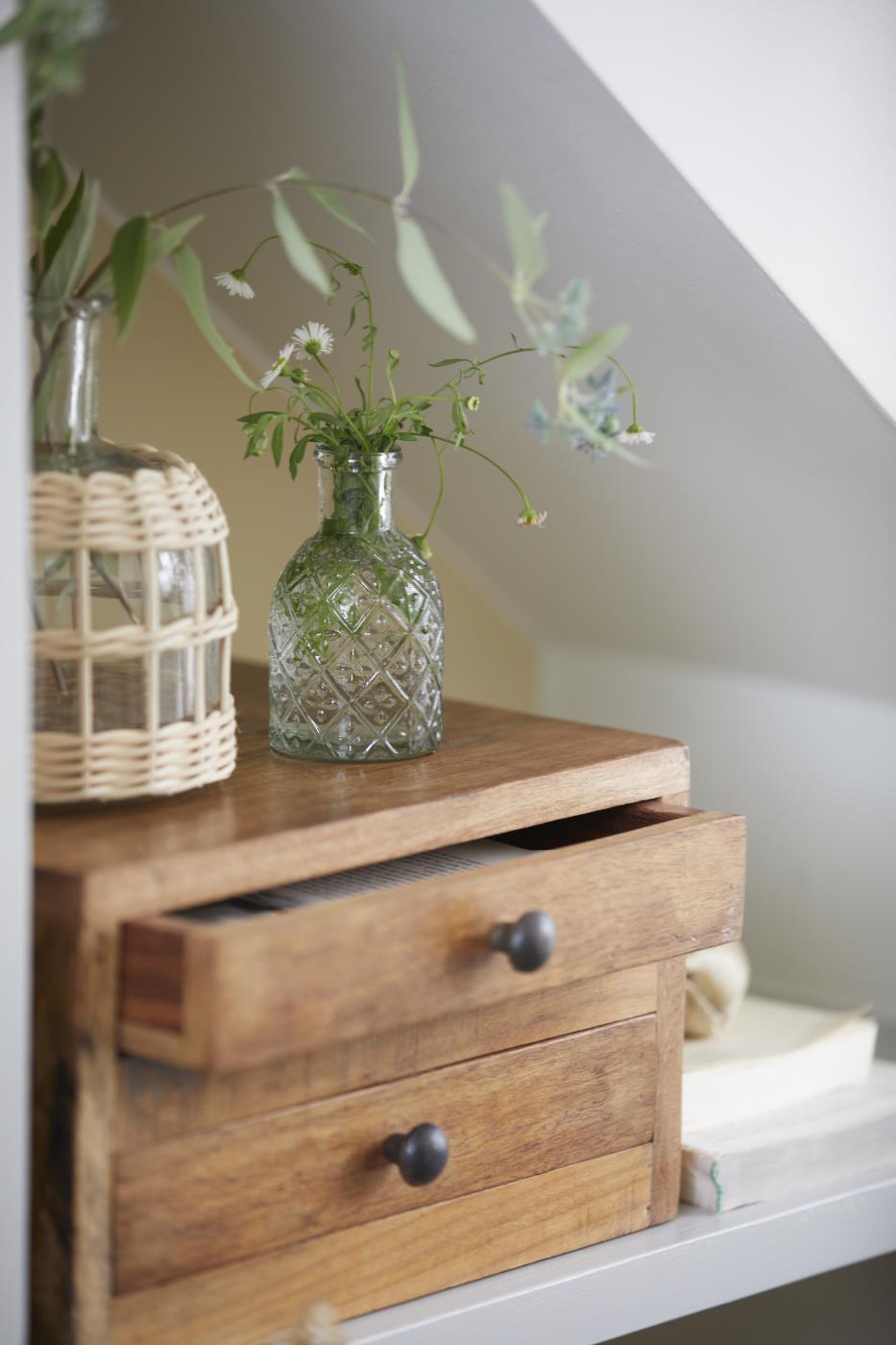 Apotekerglass med grønne greiner som liten vase på en trekommode