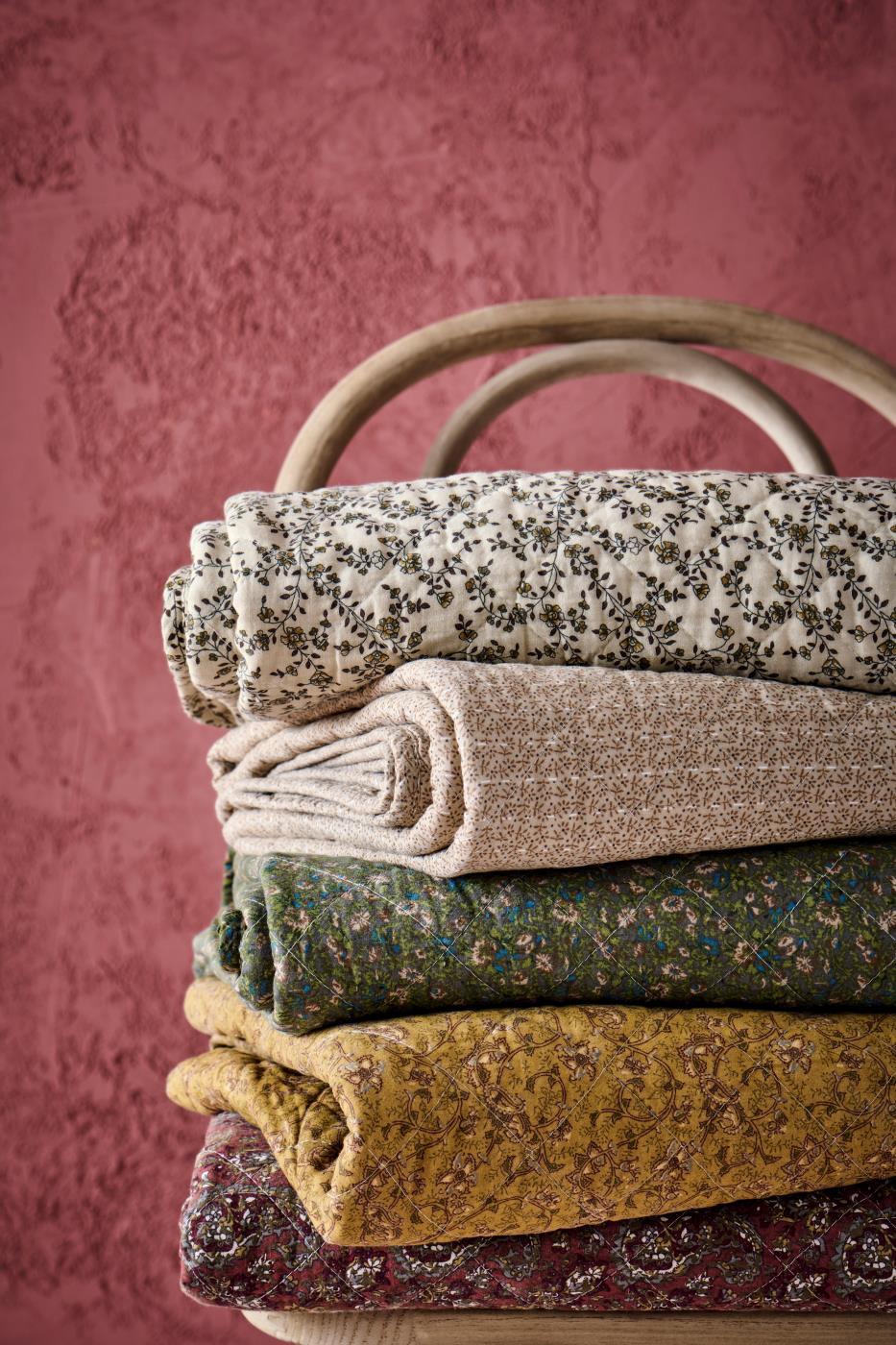 Stabel med blomstrete og mønstrete quilts fra Ib Laursen i varme og dempede farger