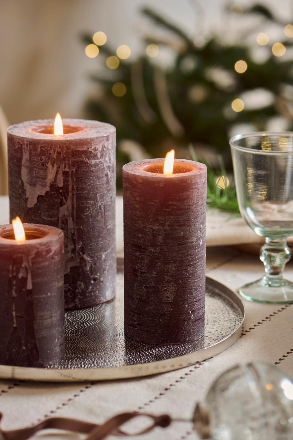Sjokoladebrune kubelys med levende flammer på dekorasjonsfat ved stemningsfullt julebord