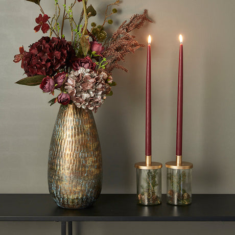 Gullfarget vase i metall med kunstige blomster ved siden av to lysestaker fra Speedtsberg