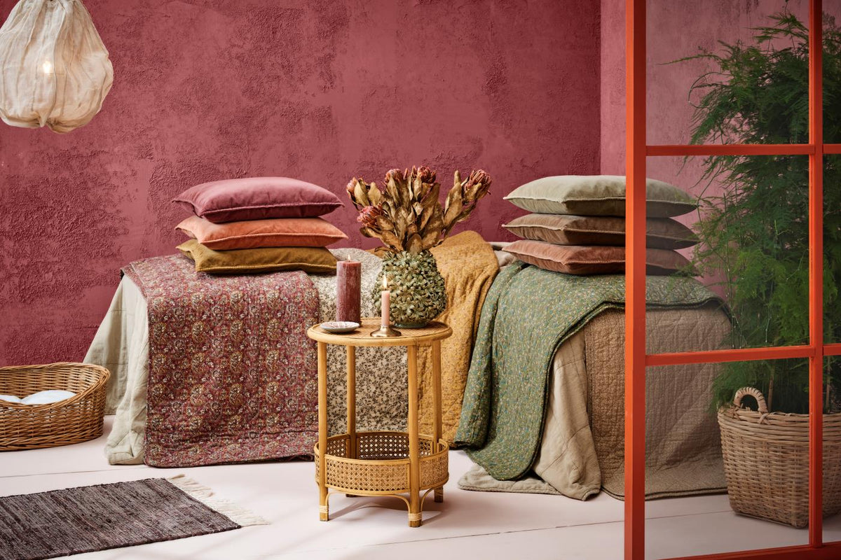 Brettede quilts og puter fra Ib Laursen i forskjellige farger og mønstre ved en rosa vegg