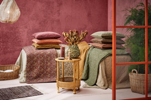 Brettede quilts og puter fra Ib Laursen i forskjellige farger og mønstre ved en rosa vegg