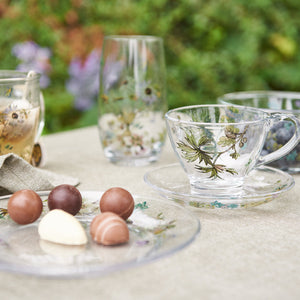 Blomstret glasskopp med underkopp fra Speedtsberg på et sommerlig kaffebord med matchende glass og små sjokolader.