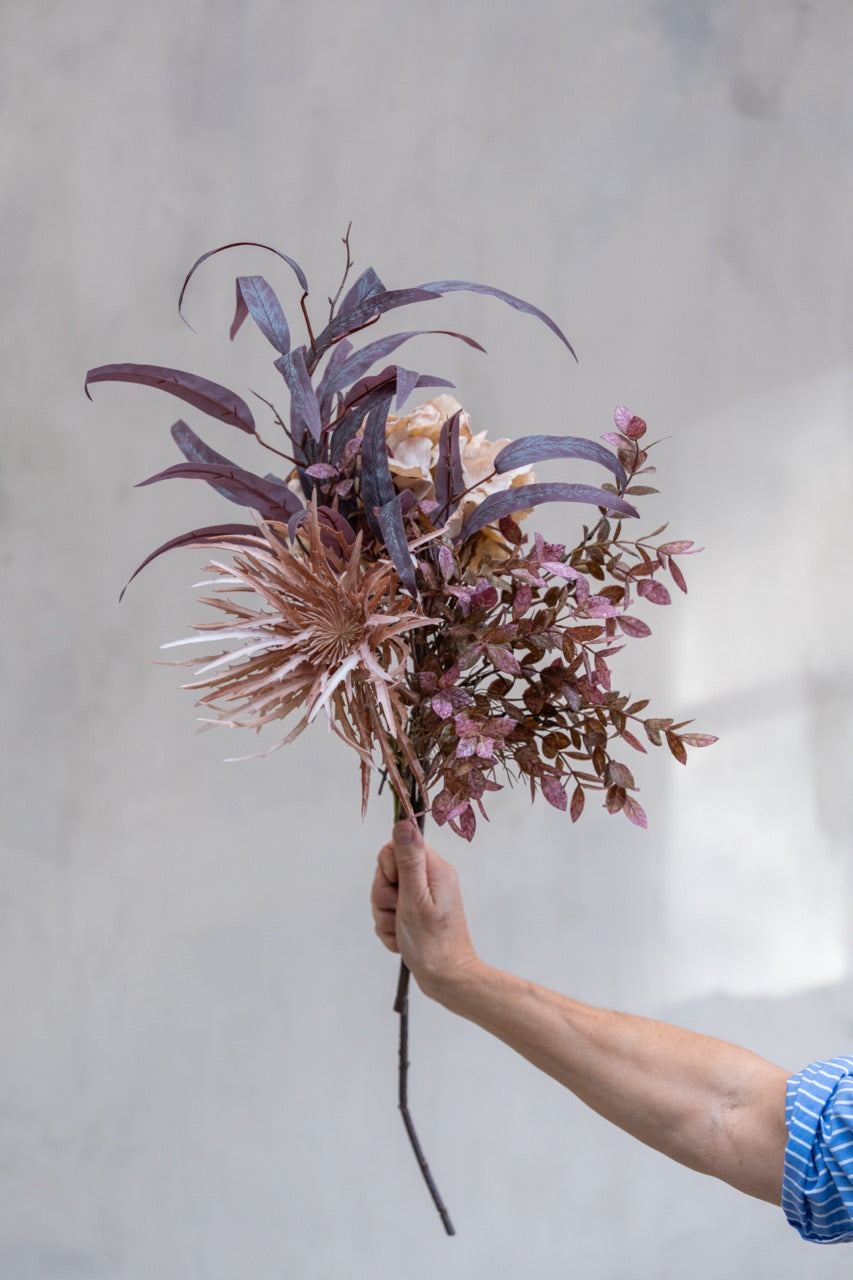 Kunstige høstblomster og eukalyptus samlet i en luftig bukett med rosa, lilla og brunlige nyanser.