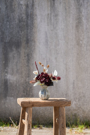 Kunstige høstblomster og dekorative greiner arrangert i en liten vase på en rustikk treskammel.