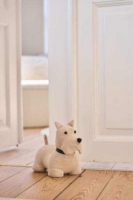 Dørstopper i hvitt og beige formet som en skottehund fra Speedtsberg som holder en hvit dør