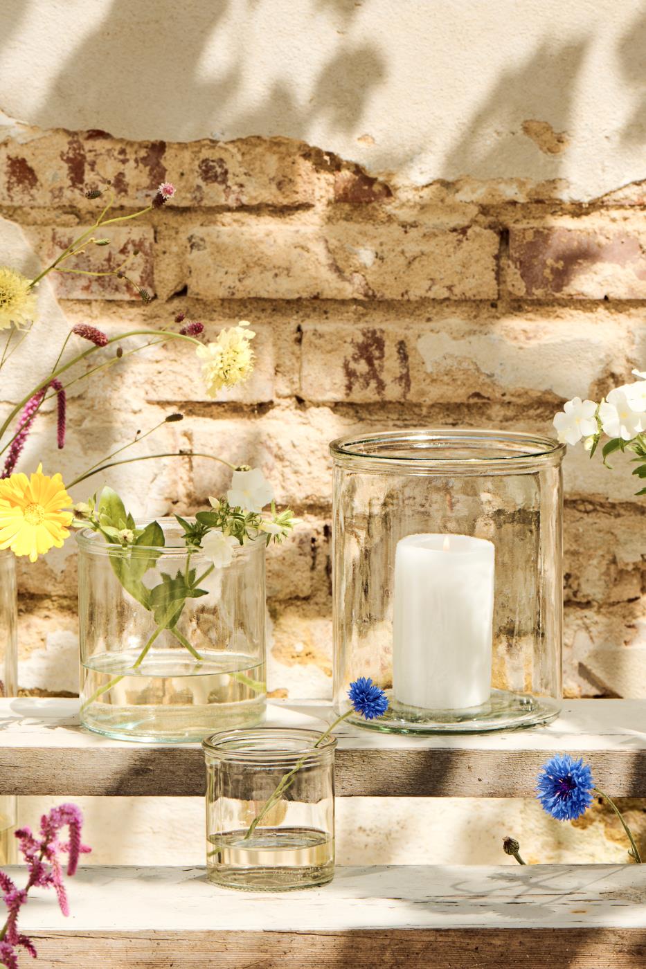 Klart Hannah sylinderglass fra Ib Laursen med hvitt blokklys blant små glassvaser og blomster