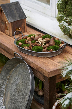 Oval Urban Garden-brett med mose, kongler og naturmaterialer som vinterdekorasjon på et trebord