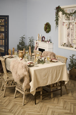 Naturfarget duk fra Ib Laursen på et koselig julebord med grønne greiner, lysestaker og klassisk julepynt