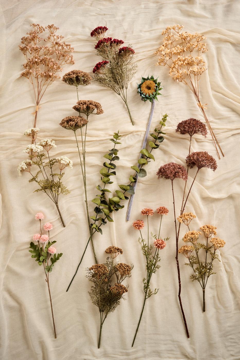 Kunstige høstblomster fra Ib Laursen i brune, rosa og gyldne naturfarger arrangert på lyst stoff.