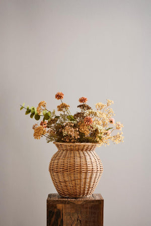 Høstbukett med kunstig eukalyptus og blomster i gyldne, brune og kremfargede nyanser i flettetvase.